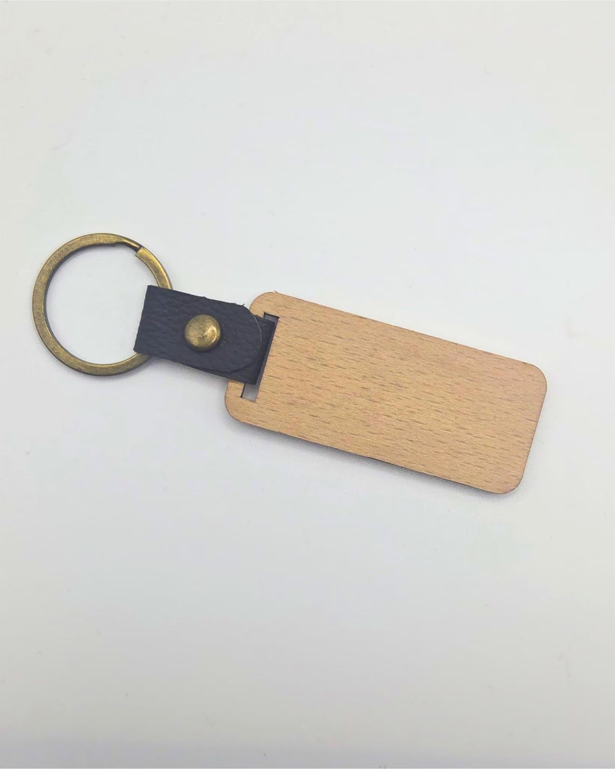 A blank wooden keychain tag with a light oak finish, attached to a black leather strap and an antique brass key ring, shown on a plain white background.