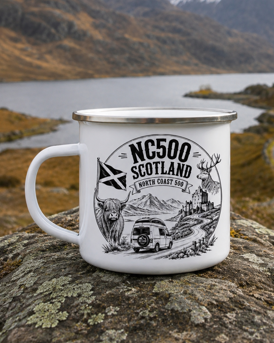 A white enamel camping mug with a silver rim and black graphic print reading 'NC500 SCOTLAND NORTH COAST' with a van, mountains, and deer, placed on a rock with a scenic mountain lake background.