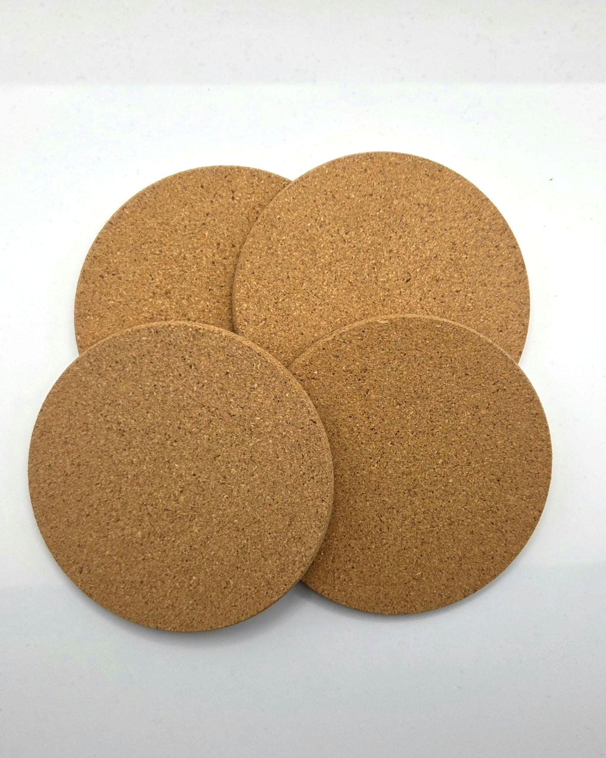 Four round cork coasters in natural tan-brown, arranged overlapping on a plain white background.