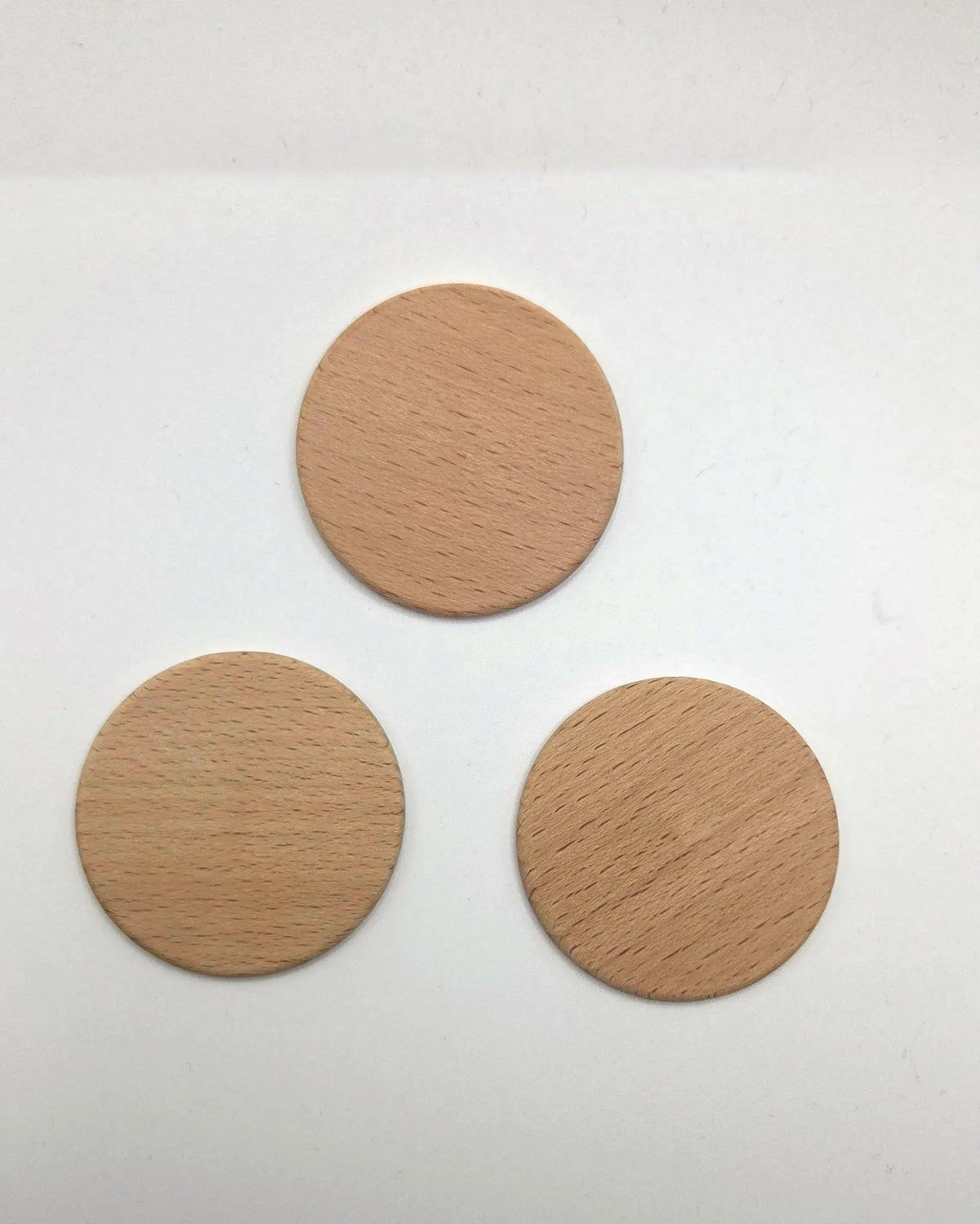 Three round light wood discs with visible grain, arranged in a triangle on a plain white background.